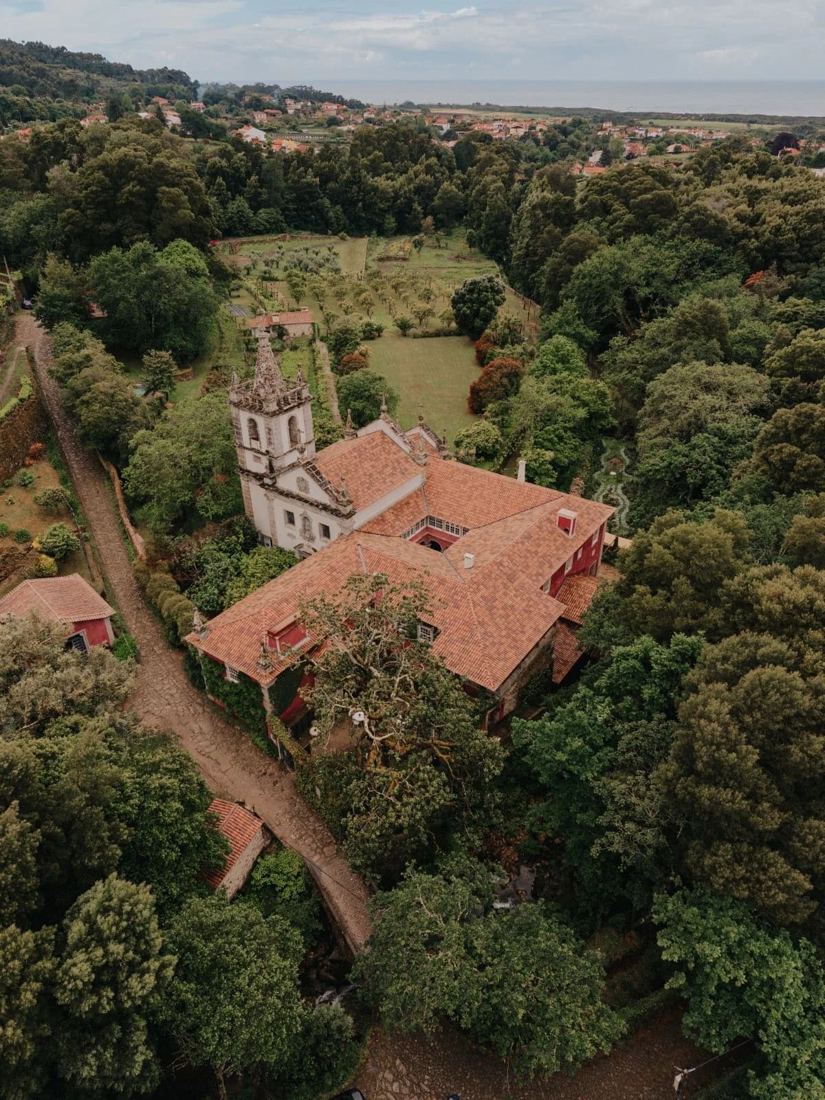 Le Convento vu du ciel : l’église, les toits du cloître et le verger, le village et l’Atlantique au loin