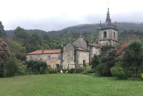 An archival photograph of the monastery before restoration, church and bell tower intact, the red house still derelict