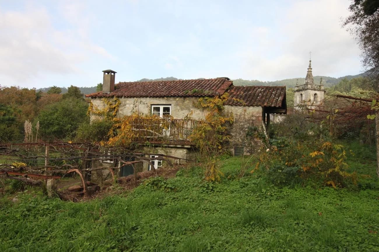 The same farmhouse derelict and overgrown, the church tower rising behind it before the restoration