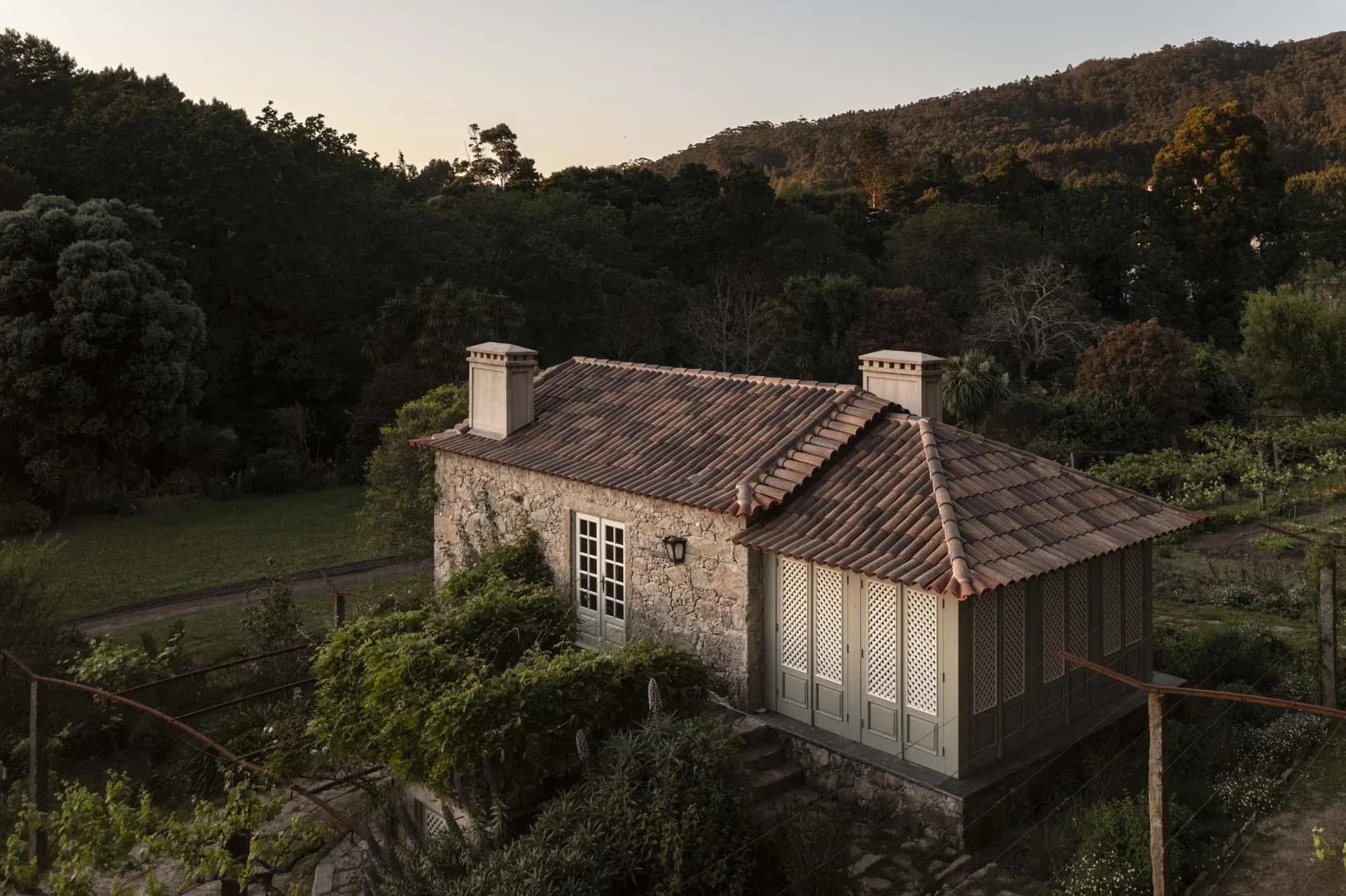 The restored farmhouse cottage at dusk, its terracotta roof and lattice shutters against the hillside