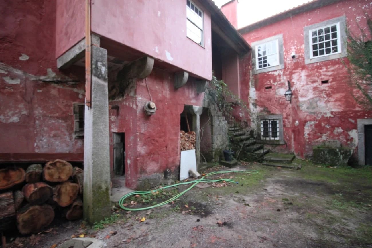 The red house courtyard before restoration, its render peeling and firewood stacked in the doorway