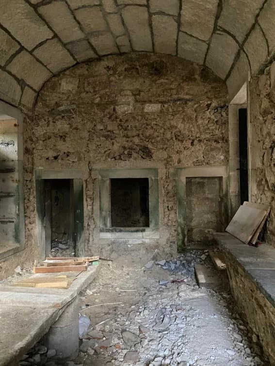 A vaulted room stripped bare before restoration, stone walls exposed and rubble on the floor
