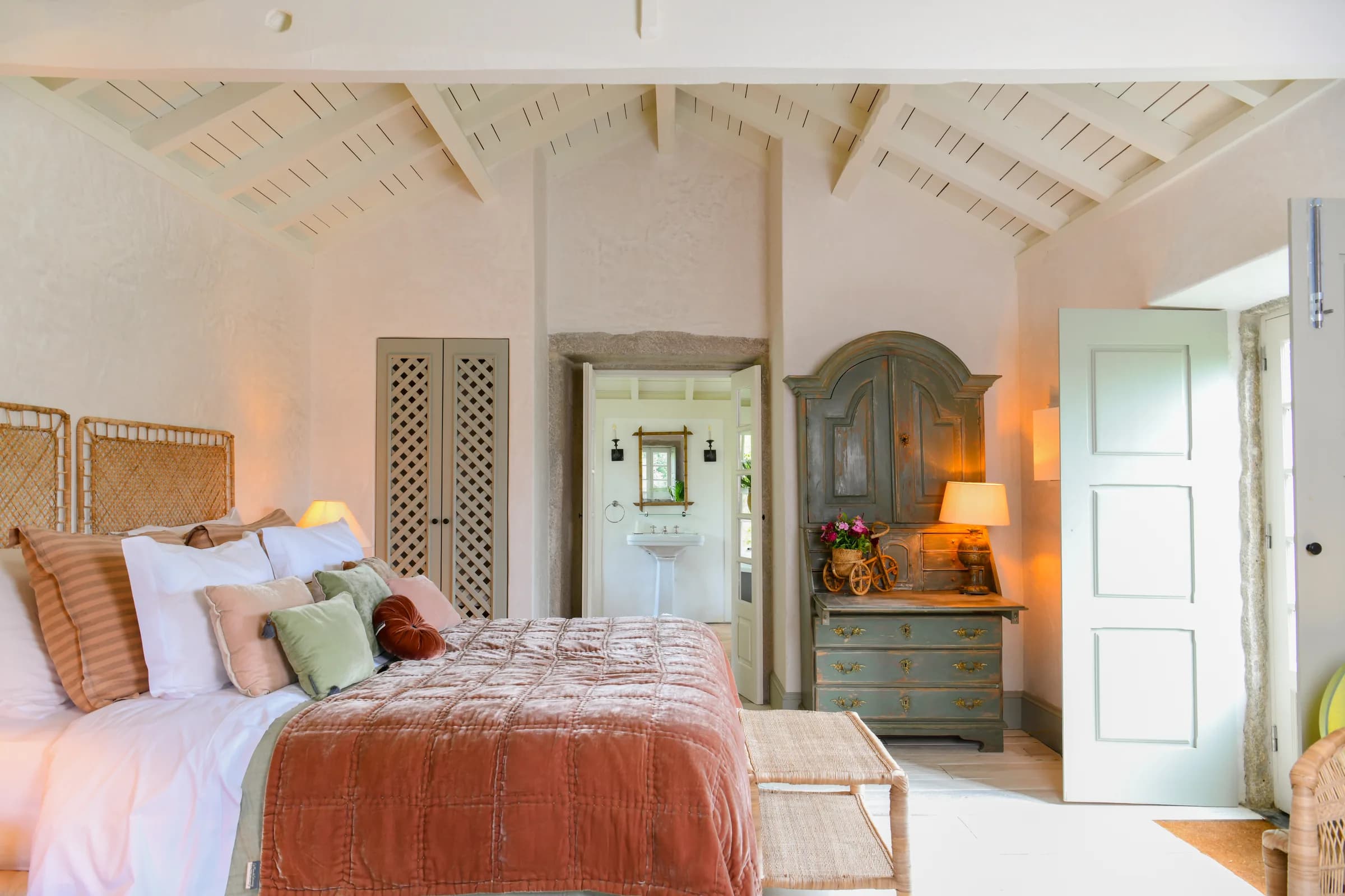 The Capucine suite — the bed beneath the vaulted timber ceiling, doors ajar to the bath