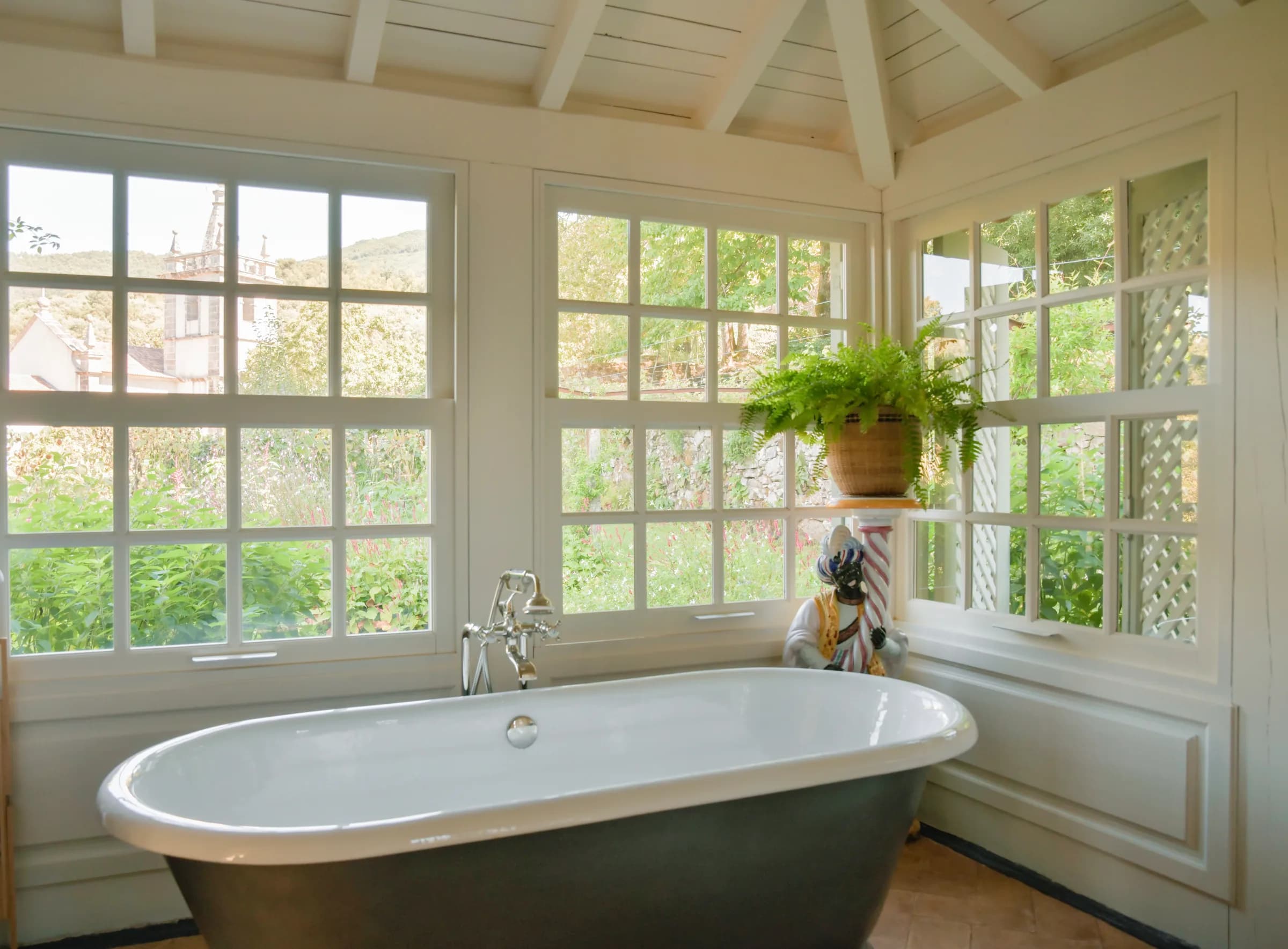 The Capucine bathroom — the freestanding tub beside a potted fern and garden windows