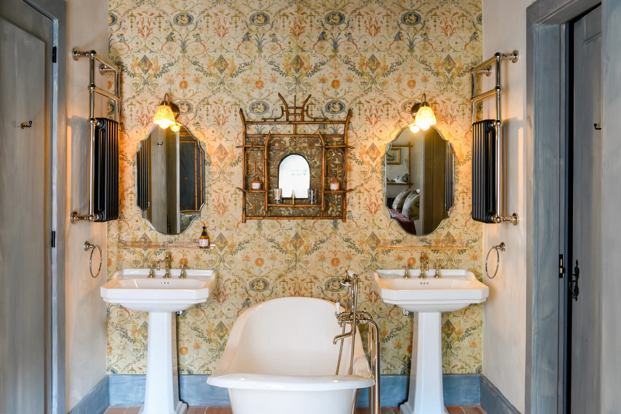 The Dahlia bathroom — twin pedestal basins beneath gilt wallpaper