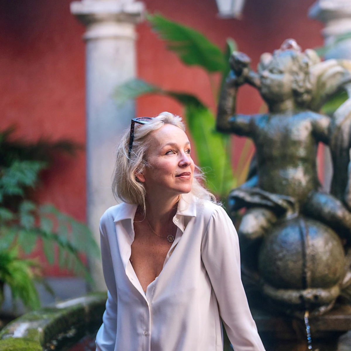 Nathalie d'Ornano seated by the cloister fountain, beneath the rose-washed arcades