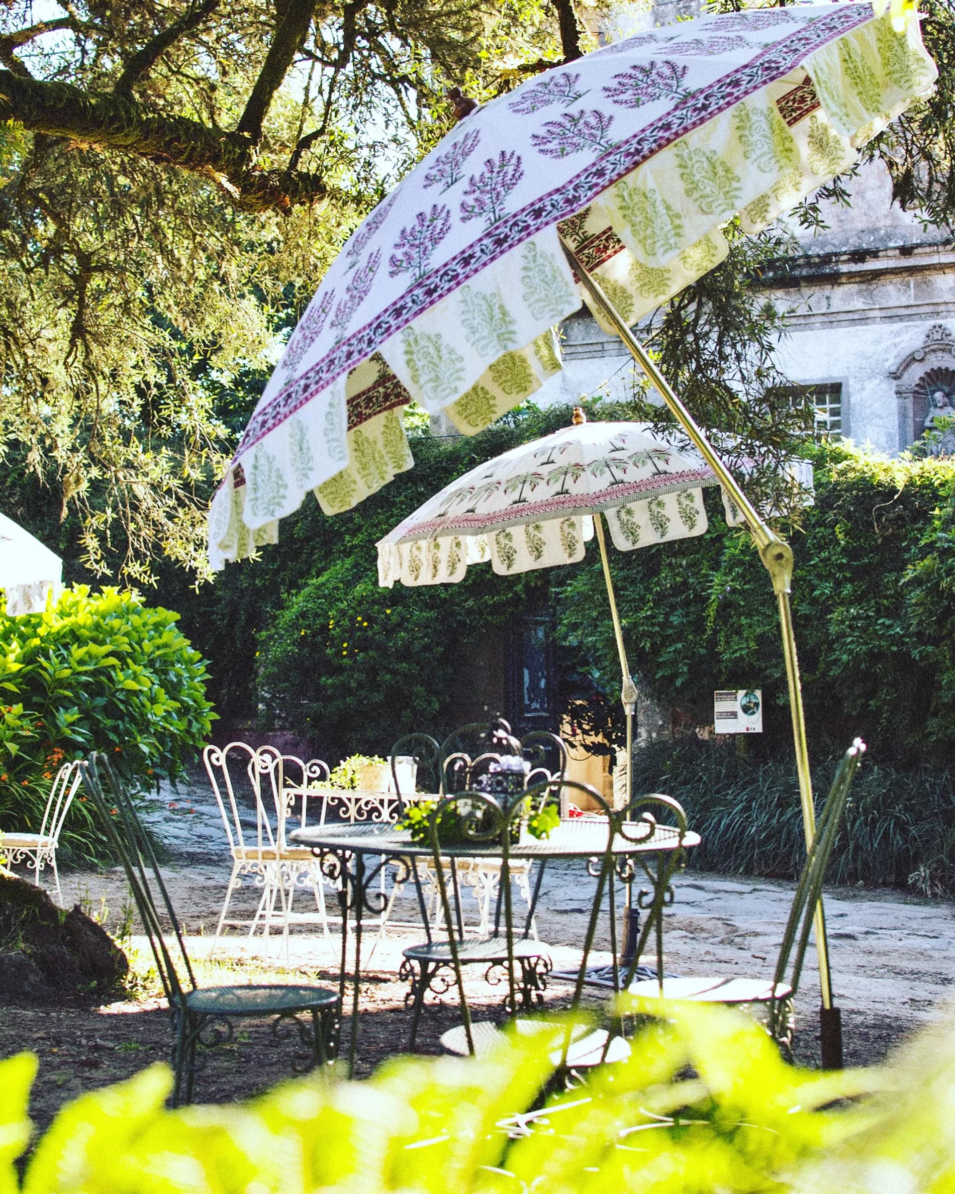 Floral garden umbrellas catching the afternoon light over the café's stone tables