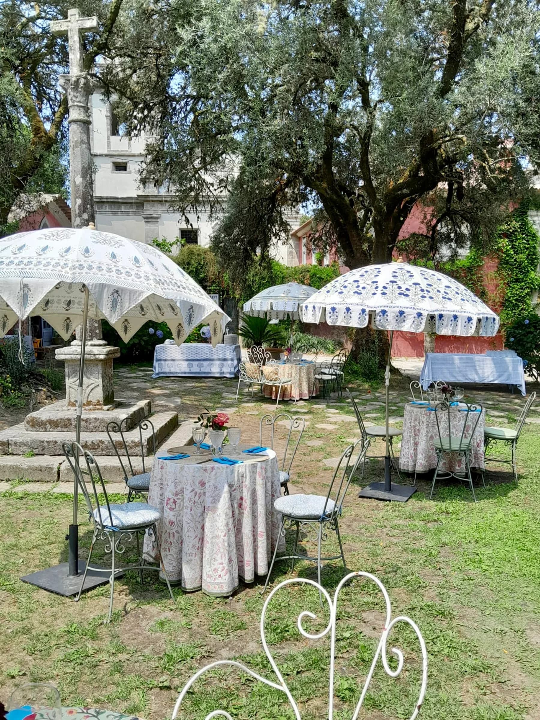 Café de Cabanas — block-print garden umbrellas over set tables, beneath the old cross and the church tower