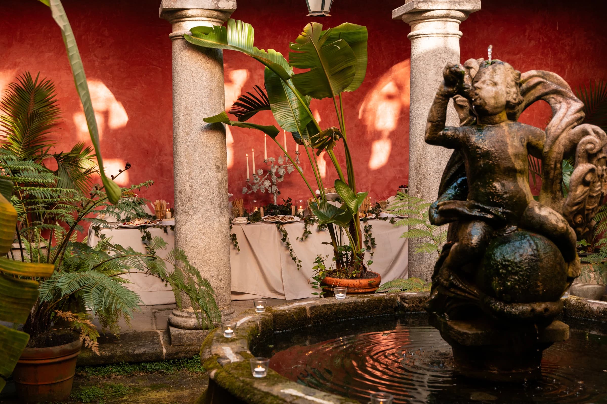 The convent's cloister by candlelight, a stone fountain statue beside tables dressed for a reception