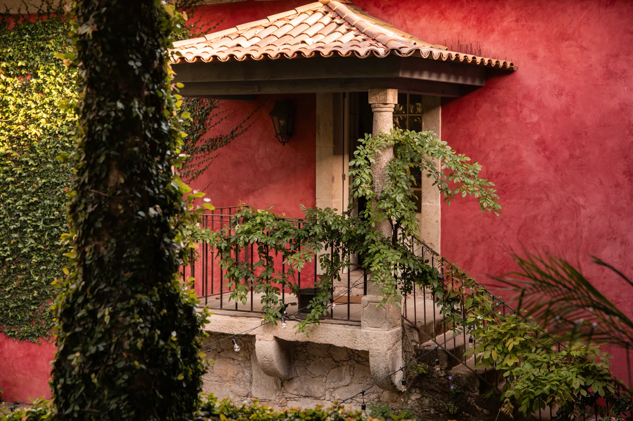 The red garden pavilion's tiled roof and stone column, wisteria climbing its rail