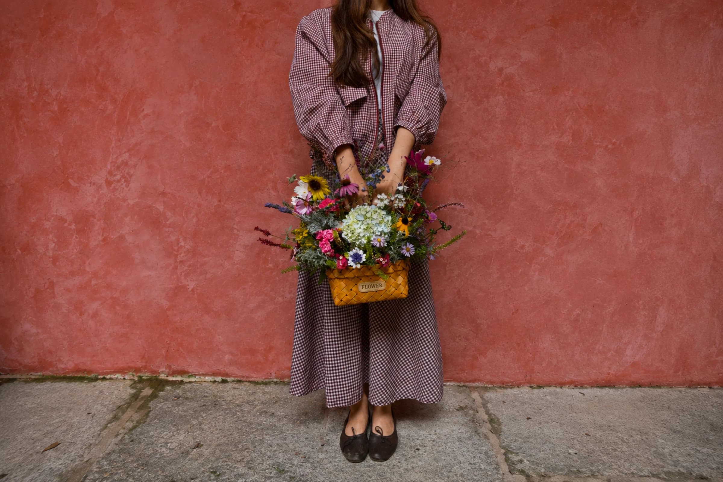 A guest holding a woven basket brimming with freshly cut wildflowers against a terracotta wall