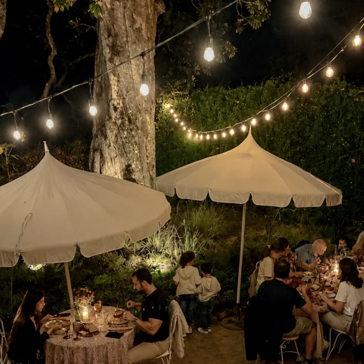 A garden dinner under parasols and string lights at dusk